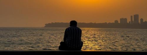 a man sitting on the beach watching the sunset at THE HEART OF HEAVEN in Āmbavna