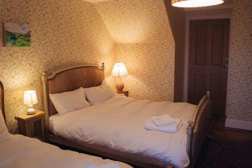 a bedroom with two beds and two lamps and a door at Claggan Farmhouse, Loch Tay in Aberfeldy