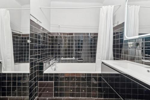 La salle de bains est pourvue de carrelage noir, d'une baignoire et d'un lavabo. dans l'établissement Magnifique appartement au cœur du 6ème, à Lyon