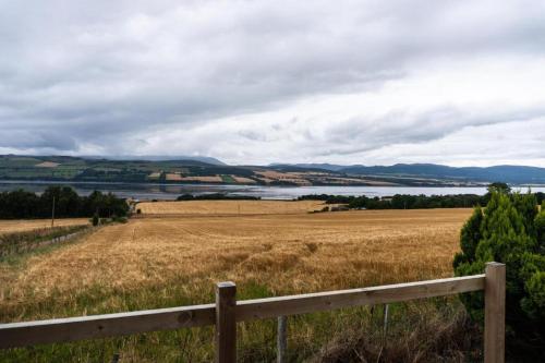 a field with a fence in front of a lake at Culbokie Lodges in Culbokie