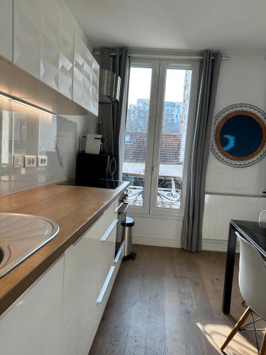 une cuisine avec des placards blancs et une grande fenêtre dans l'établissement Charmant 2P lumineux aux portes de Paris, à Ivry-sur-Seine