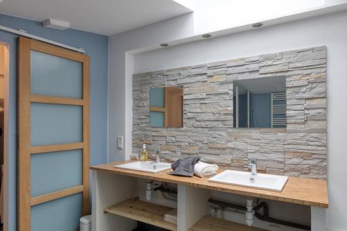 La salle de bains est pourvue de 2 lavabos et d'un mur en pierre. dans l'établissement L'Escale Maison Bleue proche chantiers atlantique, à Saint-Nazaire