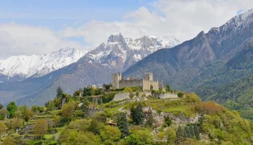 a castle on a hill with mountains in the background at Elegance Mountain Attic with sauna Edolo Ponte di Legno in Edolo