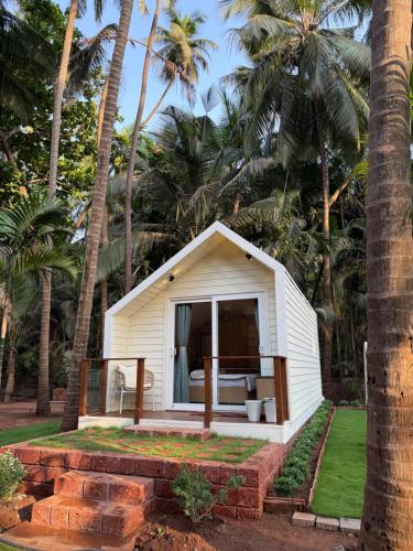 a small white shed with a porch and palm trees at Sea Breeze, Guhagar in Guhagar