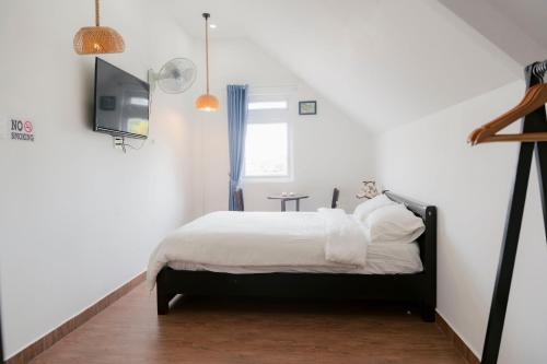 a bedroom with a bed with white sheets and a tv at Michelia Valley Hotel in Da Lat
