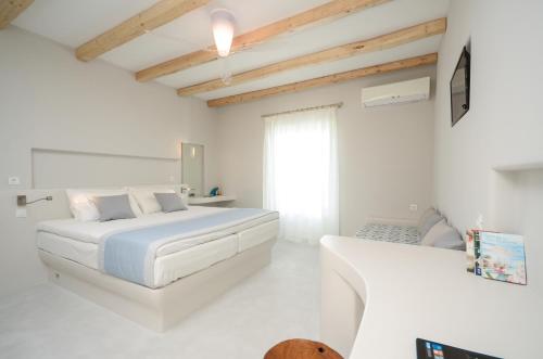 a white bedroom with a bed and a window at Antony Suites (Adults Only) in Naxos Chora