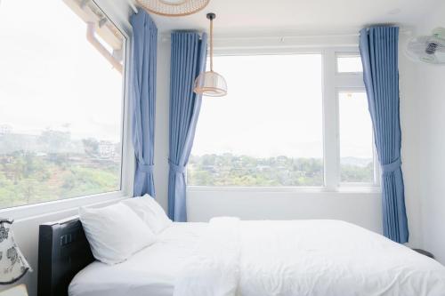 two beds in a bedroom with blue curtains and a window at Michelia Valley Hotel in Da Lat