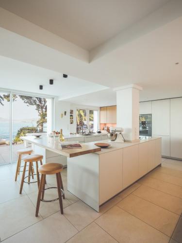 une cuisine avec des armoires blanches et un comptoir avec des tabourets dans l'établissement Villa d'exception Cala Fornaccia, à Porticcio