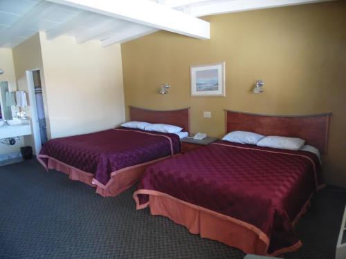 two beds in a hotel room with purple sheets at Trails Motel in Lone Pine