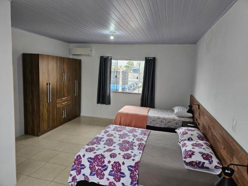 a bedroom with two beds and a cabinet and a window at Casa no centro de Navegantes in Navegantes
