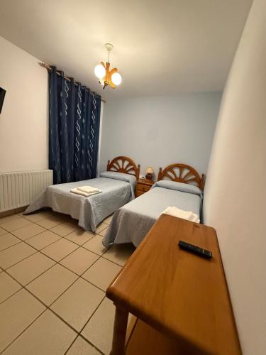 a room with two beds and a wooden table at Nuevo Hostal Rasil in Nohales