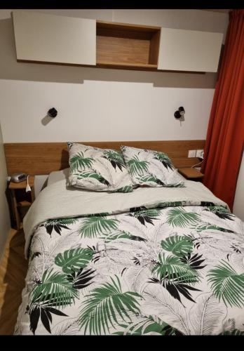 a bed with a white comforter with green leaves at mobil home in La Celle-sous-Gouzon