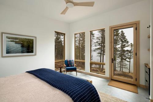 a bedroom with a bed with a ceiling fan and windows at Tallens Stuga Luxury Cabin of the Pines in Lutsen