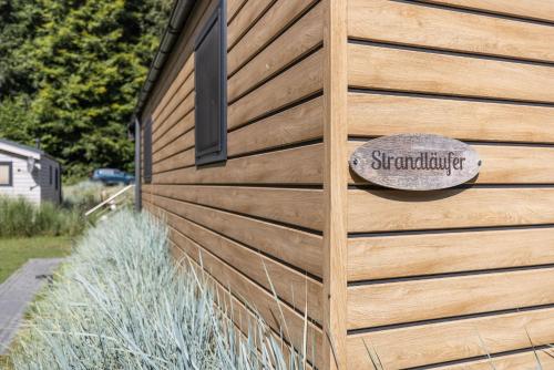a building with a wooden wall with a sign on it at Ferienhäuser Lübecker Bucht Ferienhaus Strandläufer in Haffkrug