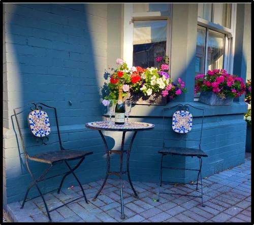 a table and chairs in front of a blue house with flowers at Coastal Cwtch in Moffat
