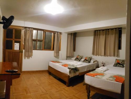 a bedroom with two beds and a table and windows at Manu Gallito de las Rocas in Pillcopata