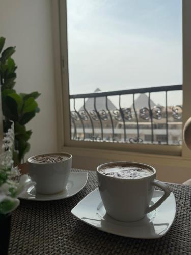 two cups of coffee on a table in front of a window at Tiye Pyramids Hotel in Cairo