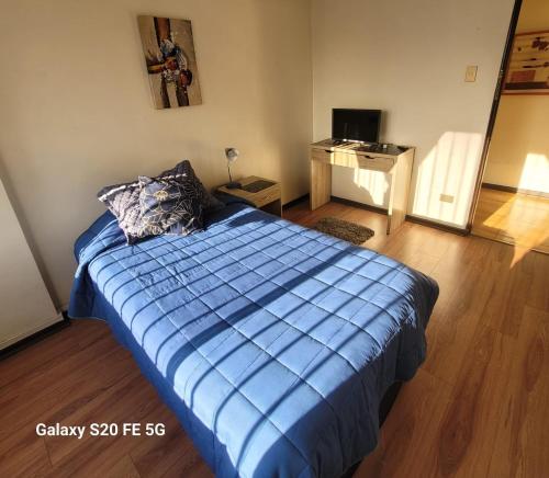 a bedroom with a bed with a blue comforter and a desk at Hostal Donde Gabriel in Chillán
