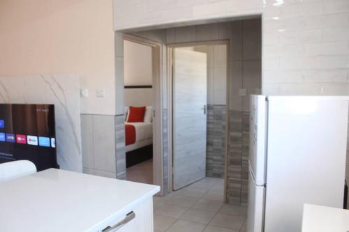 a white kitchen with a refrigerator and a bedroom at JTown CBD Self-Catering Apartment in Jwaneng