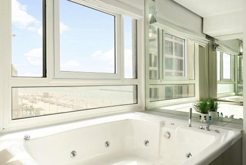 a white bath tub in a bathroom with two windows at Trumpeldor 1 - Luxury Beach Apartments Hotel - By Vacay in Tel Aviv