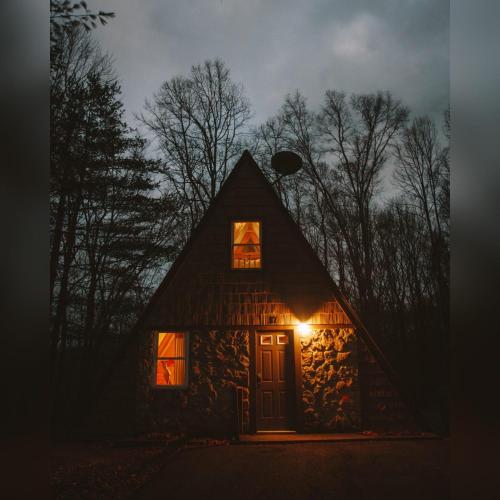 a cabin lit up at night with a light at the door at A-Frame #07 - by The Chalets in Logan