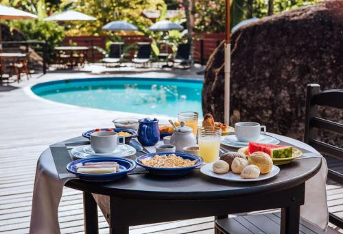 a tray of breakfast food on a table next to a pool at Pousada Vila das Pedras in Ilhabela