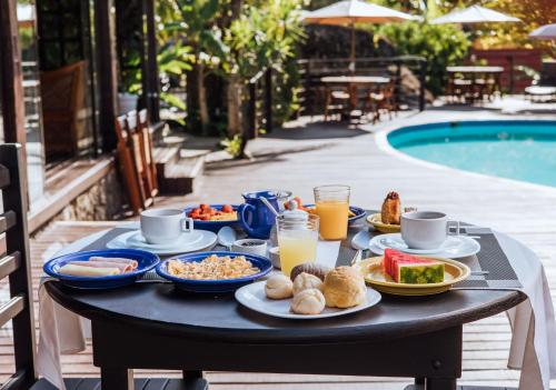 a table with breakfast food and drinks next to a pool at Pousada Vila das Pedras in Ilhabela