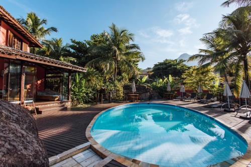 a swimming pool in front of a house with palm trees at Pousada Vila das Pedras in Ilhabela