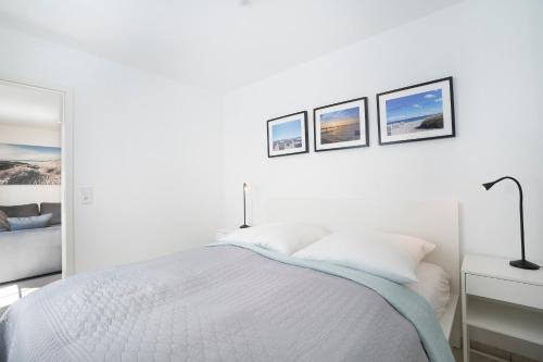a white bedroom with a bed and three pictures on the wall at Haus Titania Wohnung 2 in Grömitz