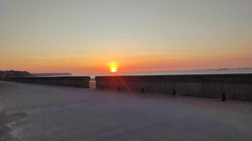 a sunset on the beach with the sun in the distance at Le Belle Vue d'Asnelles chez Lisa & Clément in Asnelles