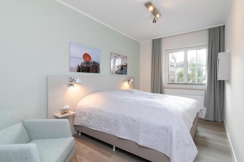 a white bedroom with a bed and a chair at Seepark Strandglück in Scharbeutz