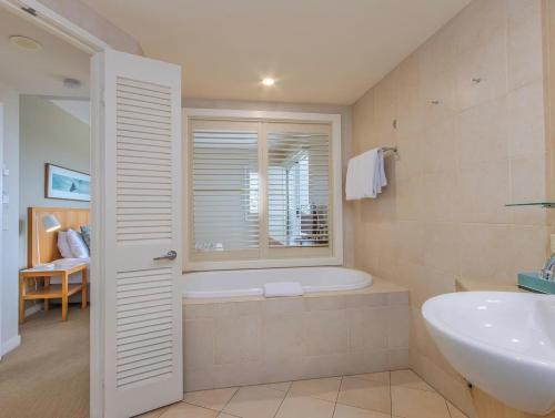 a bathroom with a tub and a sink and a window at The Pool Resort Kingscliff - Private Apartments by Holiday Management Company in Kingscliff