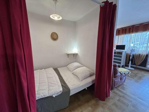 - un petit lit dans une chambre dotée de rideaux rouges dans l'établissement Studio cabine à Port Camargue, accès plage 4 pers - FR-1-250-308, au Grau-du-Roi