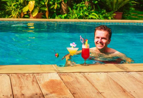 a man in a swimming pool with two drinks at Angkor Home 27 in Phumĭ Réach Born