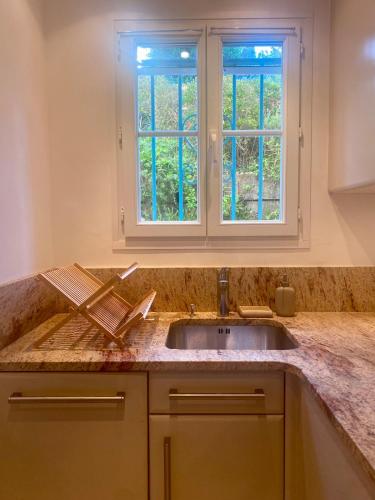 une cuisine avec un évier et deux fenêtres dans l'établissement Villa nichée sur golf & piscine, à Sainte-Maxime