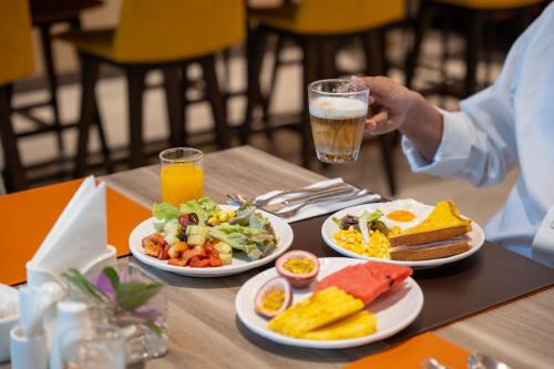 a table with two plates of food and a person holding a drink at PARKROYAL Suites Bangkok in Bangkok