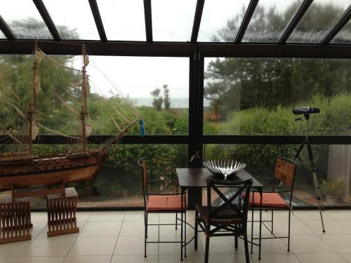 une salle à manger avec une table et un bateau à la fenêtre dans l'établissement Les Jardins d'Omaha, à Saint-Laurent-sur-Mer