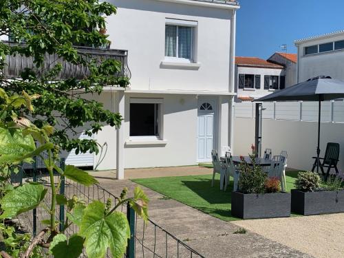 une maison blanche avec une cour dotée de chaises et d'un parasol dans l'établissement Maison familiale, à La Tranche-sur-Mer