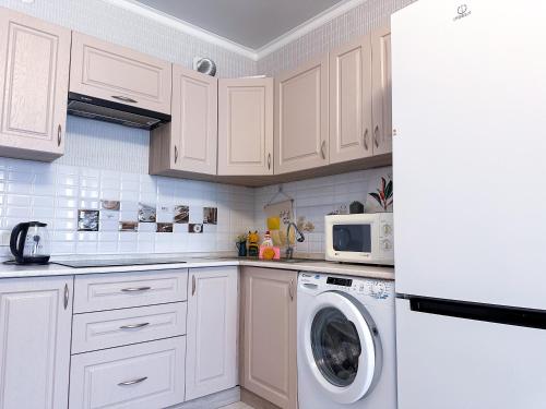 a kitchen with white cabinets and a washer and dryer at Уютная студия в центре города in Almaty