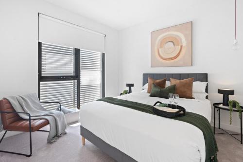 a white bedroom with a large bed and a chair at Urban Living at Its Best in Carnegie