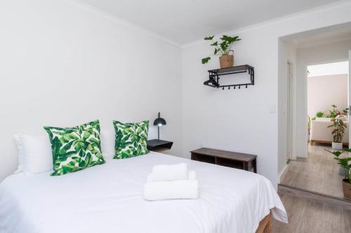 a white bedroom with a white bed with green pillows at Tranquil Flatlet in Seapoint in Cape Town