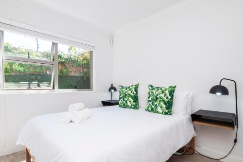 a white bedroom with a white bed with green pillows at Tranquil Flatlet in Seapoint in Cape Town