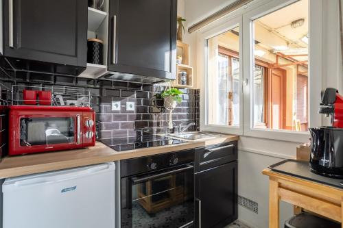 a kitchen with black cabinets and a red microwave at Appartement de charme, Maison des examens, Paris ligne 14 in Gentilly