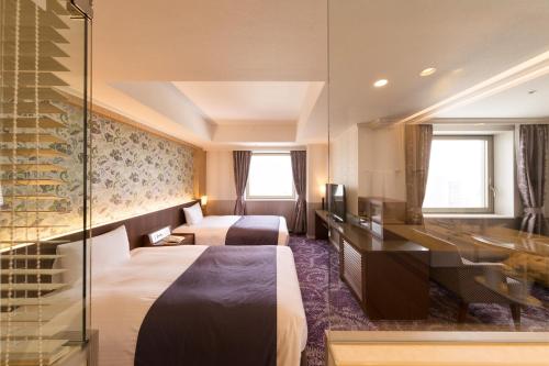 a hotel room with two beds and a desk at Kokusai 21 International Hotel in Nagano