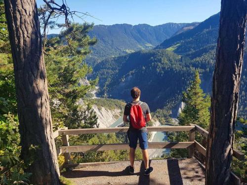 a man with a red backpack standing on a ledge overlooking a valley at Via Valla - Spacious Open-plan and Peaceful Chalet in Salums in Laax