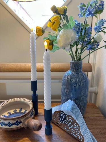 two white candles on a table with a vase of flowers at Skuespiller Centralen in Viborg