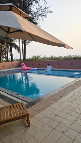 a swimming pool with an umbrella and a bench at Sea Breeze, Guhagar in Guhagar