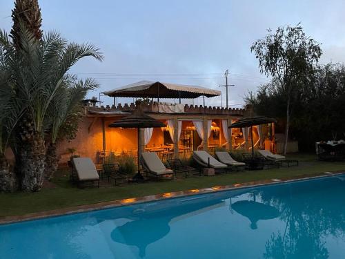 a pool with chairs and umbrellas next to a house at La Ferme Berbere Adult only in El Harkat
