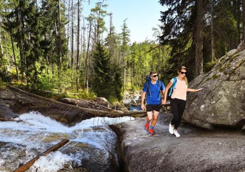 two people walking across rocks in a river at Horská ubytovňa Hrebienok in Smokovce