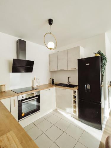 une cuisine avec des armoires blanches et un réfrigérateur noir dans l'établissement Cocon urbain proche La Défense-Paris - logement entier, à Colombes